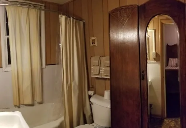 A bathroom with a tub, cream curtains and a tall carved wooden door with an arched mirror