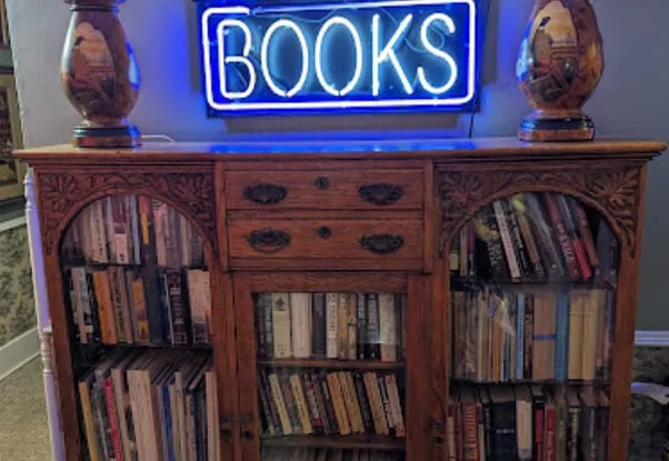 A carved antique bookcase full of books under a blue neon BOOKS sign