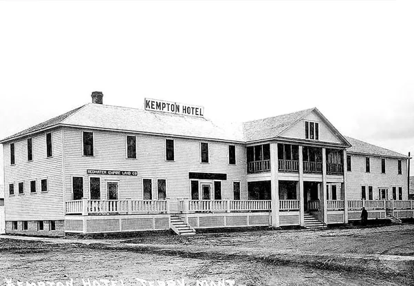 An early black-and-white photograph of the Kempton Hotel with its long front porch and its name painted on the roof