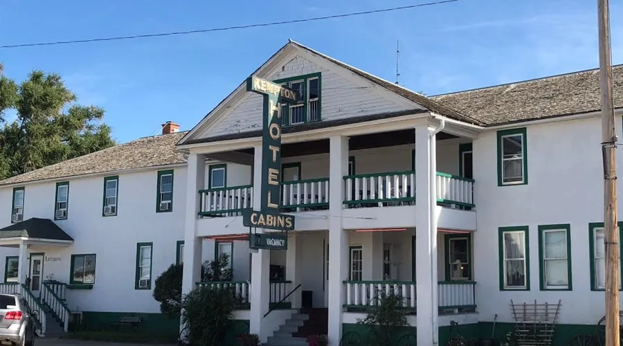 The Kempton Hotel today: white clapboard walls, green trim, double porches and a tall neon HOTEL sign