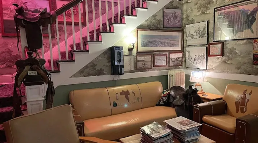 A sitting area under the stairs with a leather sofa, stacks of magazines, an old wall telephone and framed prints