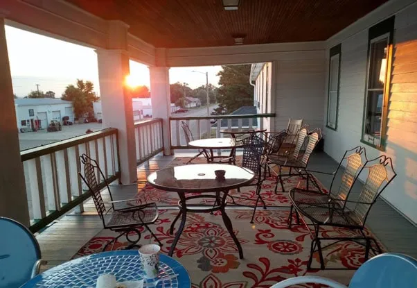 The covered porch at sunset, with iron patio tables and chairs on a red patterned rug