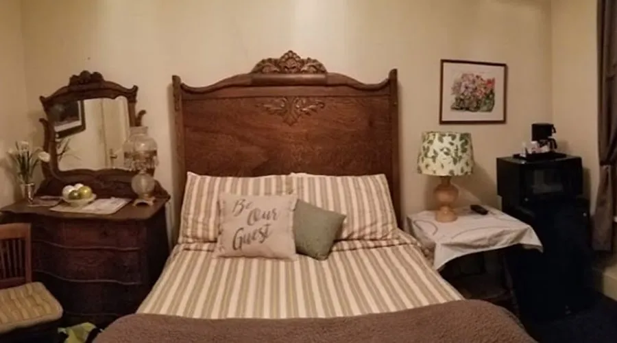 A room with a carved antique headboard, a matching dresser with a mirror, and a striped bedspread
