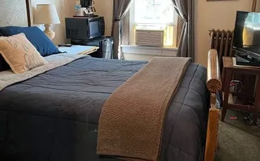 A basic room with a double bed, a blue and brown quilt, a radiator and a window air conditioner